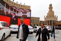 Ethnic Uyghur people walk in front of a giant screen with a picture of Chinese President Xi Jinping in the main city square in Kashgar in Xinjiang Uighur Autonomous Region, China September 6, 2018. The screen broadcasts a slideshow of images of Xi on loop