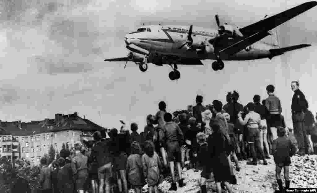 Un avion C-54 Skymaster al Forțelor Aeriene ale SUA aterizează la baza aeriană Tempelhof din Berlin, sub privirile pline de speranță ale berlinezilor, la 10 august 1948. Podul aerian a funcționat timp de 15 luni, după ce autoritățile sovietice au izolat orașul. Aproximativ 101 participanți au murit, dintre care 40 de britanici și 31 de americani, majoritatea din cauza unor accidente care nu au avut loc în timpul zborului.