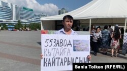 "55 зауыт Қытайға қайтарылсын!" деген жазуы бар плакат ұстап, Бəйтерек монументі алдында бір адамдық пикет өткізіп тұрған белсенді Асқар Қайырбек. Нұр-Сұлтан, 18 тамыз 2019 жыл.