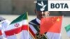 Një ushtar mban lart flamujt kombëtarë iranianë dhe kinezë gjatë stërvitjeve të përbashkëta detare midis Iranit, Rusisë dhe Kinës në portin iranian, në Gjirin e Omanit, në vitin 2019.