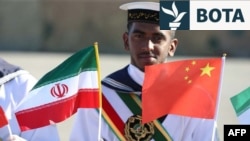 Një ushtar mban lart flamujt kombëtarë iranianë dhe kinezë gjatë stërvitjeve të përbashkëta detare midis Iranit, Rusisë dhe Kinës në portin iranian, në Gjirin e Omanit, në vitin 2019.