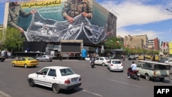 Șoferii trec pe lângă un panou publicitar uriaș pe care scrie „Strâmtoarea Ormuz rămâne închisă” în Piața Revoluției din Teheran, pe 12 aprilie 2026.