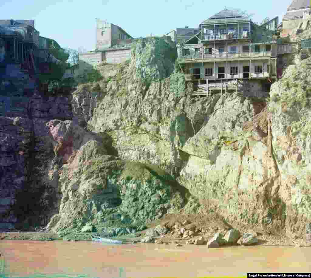 Дом на вершине скалы в Тбилиси, с опасной тропой, ведущей к реке и лодке. Из трубы справа в реку Мтквари сбрасываются сточные воды
