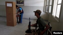 An army soldier sits by as a voter stamps his ballot papers inside a booth at a polling station during the repeat vote on May 19 in Karachi's NA-250 constituency.