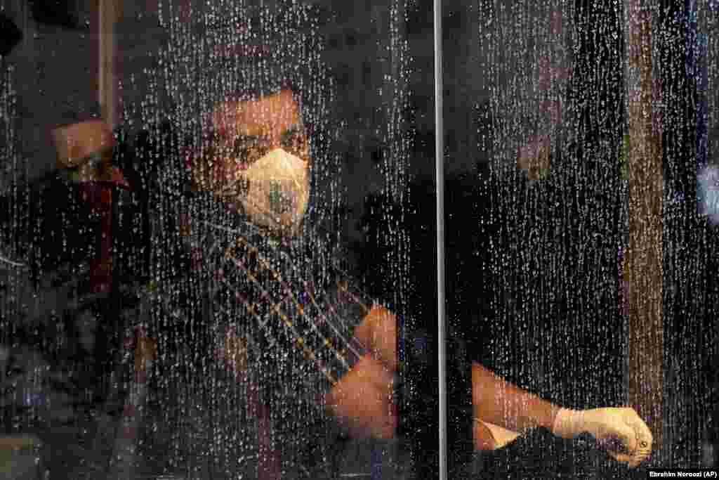 A commuter looks through a water-stained window wearing a mask and gloves to help guard against the coronavirus on a public bus in downtown Tehran. Iran&#39;s Health Ministry raised the death toll from the new virus to 12 people in the country on February 25, amid concerns that clusters there, as well as in Italy and South Korea, could signal a serious new stage in its global spread. (AP/Ebrahim Noroozi)