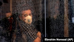 A commuter looks through a water-stained window wearing a mask and gloves to help guard against the Coronavirus, on a public bus in downtown Tehran, February 23, 2020