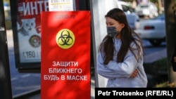 Девушка в маске проходит мимо знака, предупреждающего об опасности коронавируса