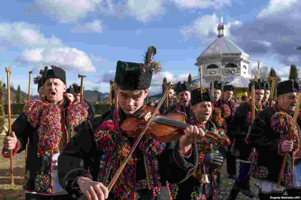 A young man plays the violin as others, all wearing traditional dress, sing during Orthodox Christmas celebrations in western Ukraine. (AP/Yevgeniy Maloletka)