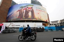 Un bărbat pe motocicletă privește un panou publicitar cu noul lider suprem al Iranului, Mojtaba Khamenei, în Teheran, pe 12 martie 2026.