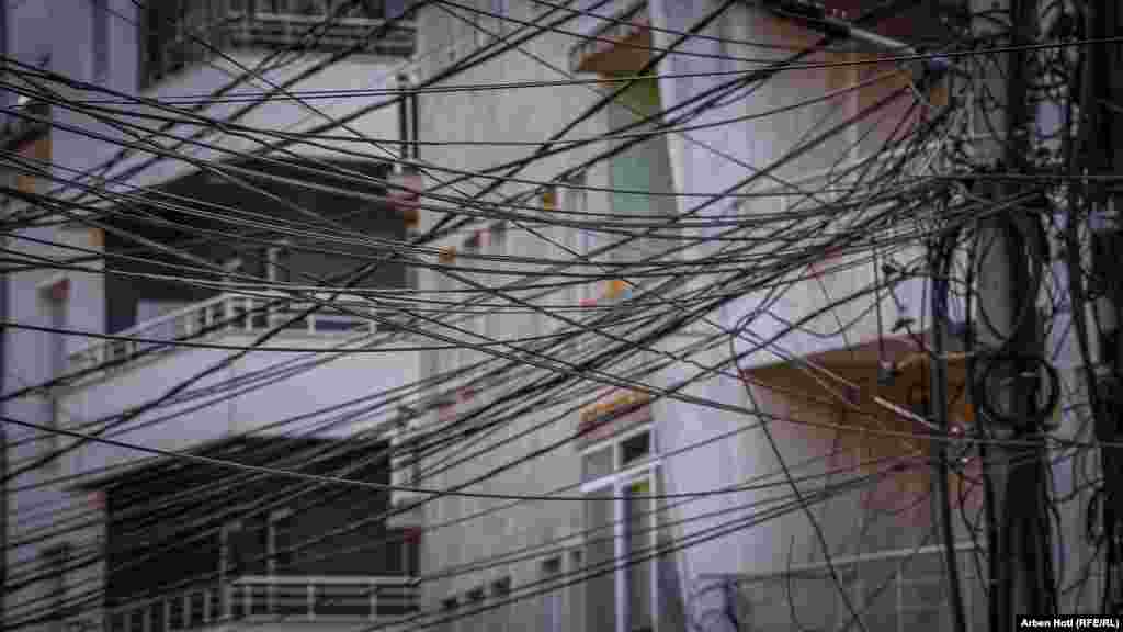 Kabllo të shumta ajrore të vendosura në mënyrë kaotike pranë ndërtesave të banimit në lagjen "Dodona" në Prishtinë.Infrastruktura e rrjetit të komunikimeve dhe energjisë ka qenë kaotive prej vitesh në kryeqytet, edhe pse ka lagje që kanë filluar t'i heqin shtyllat dhe të kalojnë në rrjet nëntokësor.