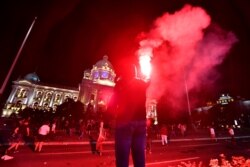 A protester holds a flare as Serbian police fire tear gas in front of the National Assembly building in Belgrade on July 7 to disperse thousands of protesters.