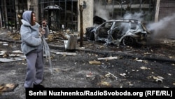 A woman carries her dog and videos the aftermath of a deadly Russian missile strike on Kyiv on December 20. 