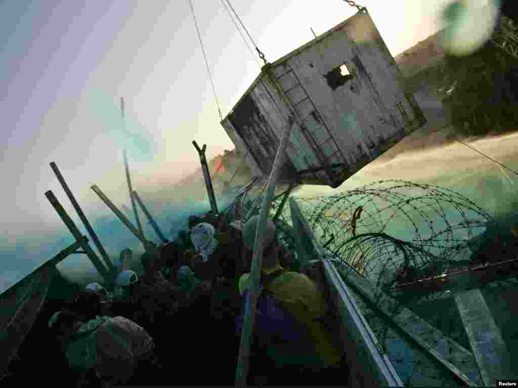 Israeli special evacuation forces arrive on the rooftop of a synagogue in the Jewish Gaza Strip settlement of Kfar Darom. Israeli special evacuation forces arrive on the rooftop of a synagogue, inside a container, in the Jewish Gaza Strip settlement of Kfar Darom on August 18, 2005. Israeli troops using cranes and water cannon fought protesters on the rooftop of a synagogue on Thursday as they assaulted the last bastions of resistance to evacuation of the occupied strip. In the most violent scenes since the start of forced evictions from Gaza, police armed only with shields poured from a cage hoisted on top of the synagogue and grappled with settlers and their supporters before dragging them away. Picture taken August 18, 2005. REUTERS/Nir Elias 