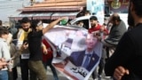 Syrian refugees hold a banner bearing a picture of President Bashar al-Assad with Arabic writing referring to him as a "pig" in the eastern Lebanese town of Majdel Anjar in the Bekaa Valley on December 8, 2024, following the fall of the Syrian capital to 