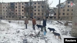 Oameni cară sticle cu apă pe lângă clădiri rezidențiale avariate în orașul Avdiivka din regiunea ucraineană Donețk, controlată de Rusia. Imagine preluată dintr-un videoclip furnizat de Ministerul rus al Apărării pe 20 februarie 2024.