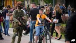 Egy orosz katona őrködik, miközben helyi civilek sétálnak Melitopol központjában, a Zaporizzsjai, orosz katonai ellenőrzés alatt álló területen 2022. május 1-jén