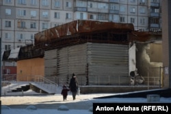 Cалтівка, мати з дитиною на фоні торгівельного майданчика, який згорів після обстрілів у 2022-му році. Харків, лютий 2026