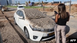 A woman takes a picture of a damaged vehicle in the aftermath of an Iranian missile attack on Israel. 