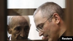 Mikhail Khodorkovsky speaks to a lawyer as he stands in the defendants' box during a court session in Moscow on May 24, 2011.