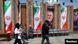 Disa persona duke kaluar pranë një baneri kushtuar komandantit të ndjerë të Gardës Revolucionare Islamike. Teheran, 21 prill 2026. 
