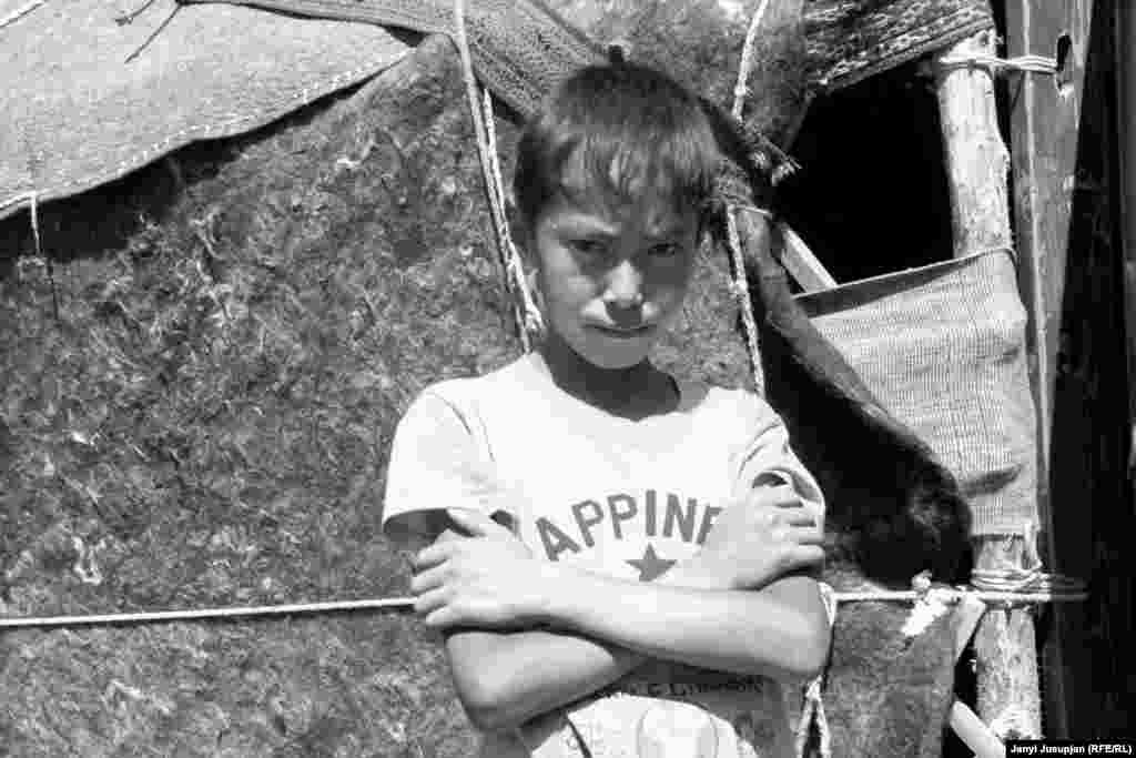 A boy stands outside a yurt. Many adult men travel for seasonal work in Kyrgyzstan or Russia, leaving women and older children to perform household duties, childcare, and agriculture work.