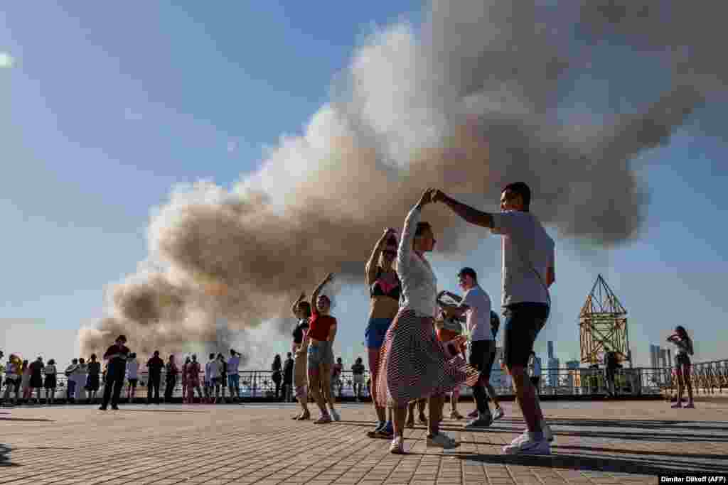 Couples dance the samba as smoke rises from a burning pyrotechnics warehouse in Moscow.