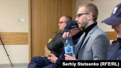 Михал Прокопович дар додгоҳ дар байни ду ходими полис нишастааст