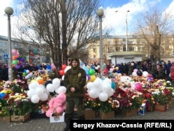 A security guard keeps an eye on an impromptu memorial to victims of the fire in Kemerovo.