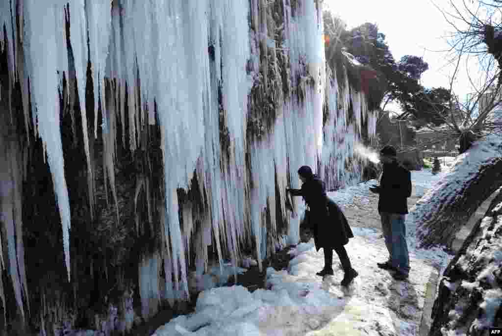 A woman breaks off a small piece of ice from giant icicles on a rock in central Tbilisi, Georgia, which was besieged by freezing weather on February 3. (AFP/Vano Shlamov)