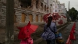 Мать и дочь, жители города Сумы, идут мимо одного из исторических зданий, поврежденного в результате российского обстрела. Фотография сделана 12 июня 2025 года