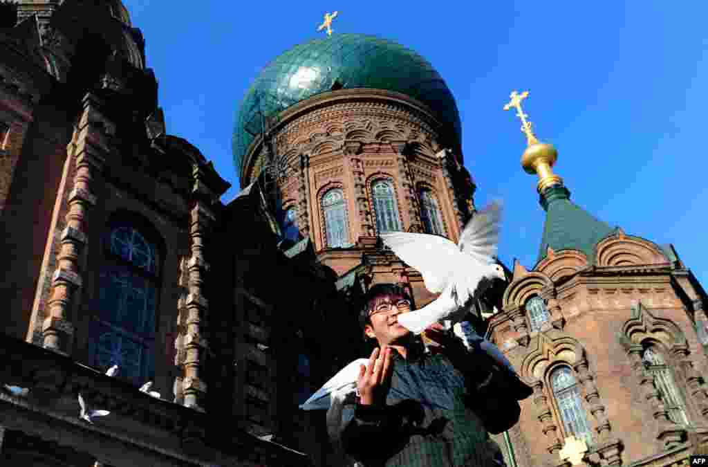 A man feeds pigeons beneath the onion dome rooftop of St. Sophia Cathedral, a former Russian Orthodox church in Harbin in northeast China. Harbin has opened a "Russian village" to attract tourists across the nearby border.