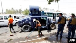 Iraqi workers clean the pavement as security forces stand guard at the site of a deadly suicide bombing near a Shi'ite shrine in Baghdad on July 24.