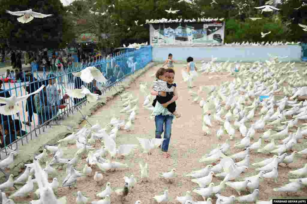 An Afghan girl holds a baby as pigeons fly overhead in the courtyard of the Hazrat-e Ali shrine, or Blue Mosque, in Mazar-e Sharif.&nbsp;(AFP/Farshad Usyan)&nbsp;
