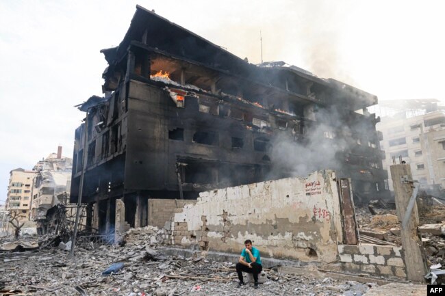 Un tânăr palestinian stă în fața unei clădiri arse în urma unor lovituri aeriene israeliene în cartierul al-Rimal din orașul Gaza, 10 octombrie 2023.