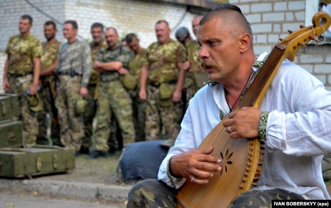 Український воїн грає на бандурі під час прощання із побратимами, які загинули у війні України з Росією. Місто Старобільськ Луганської області, 29 липня 2014 року