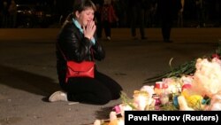 Керчьте шабуыл жасалған колледж алдына қойылған гүлдер мен шамдардың жанында отырған әйел. Қырым, 17 қазан 2018 жыл.