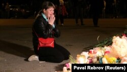 Женщина рядом с цветами и свечами, оставленными у здания колледжа в Керчи, на который было совершено нападение. 17 октября 2018 года.