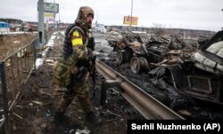 Një ushtar ukrainas qëndron pranë makinave ushtarake ruse, të cilat janë shkatërruar në Buça, pranë Kievit. 1 mars 2022.