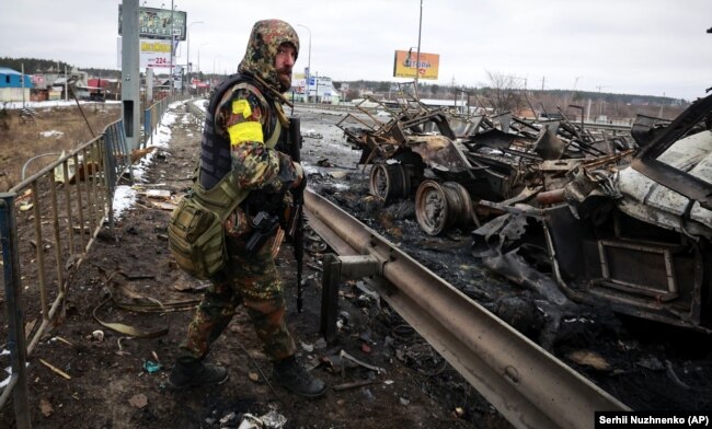 Një ushtar ukrainas qëndron pranë makinave ushtarake ruse, të cilat janë shkatërruar në Buça, pranë Kievit. 1 mars 2022.
