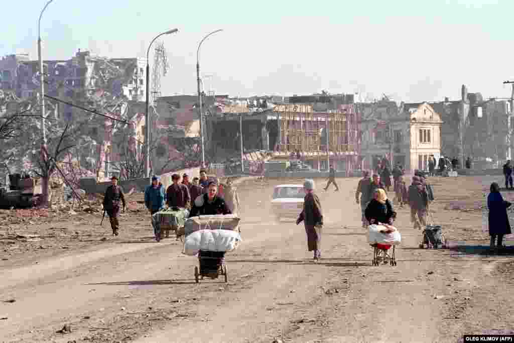 prospekt Kadyrova - formely Lenina, it is right bank of the river Sunzha, river in yours back with a view towards music school in the far back (the white building) Against a backdrop that provides a glimpse of the bombardment suffered by Chechnyans earlier this year at the hands of Russian troops and air attacks, Chechen refugees use a variety of wheeled contraptions to transport their belongings.