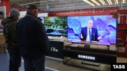 Посетители магазина бытовой техники в Крыму смотрят трансляцию пресс-конференции президента России Владимира Путина, 17 декабря 2020 года