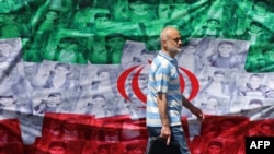 A man walks past an Iranian flag installed along a roadside on April 29 in Tehran, depicting images of children killed on the first day of the war in an alleged US-Israeli missile strike on a school in the southern Iranian city of Minab.