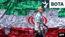 Një burrë kalon pranë një flamuri iranian ku janë vendosur portrete të fëmijëve të vrarë në ditën e parë të luftës. 