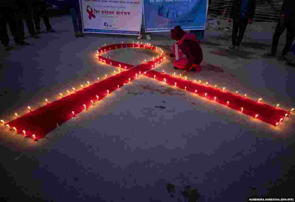 Жінки та діти &laquo;Maiti Nepal&raquo;, реабілітаційного будинку та притулку для уражених ВІЛ дітей, жінок, та жертв торгівлі людьми, запалюють свічки, утворюючи червону стрічку-символ, молячись за тих, хто втратив життя через ВІЛ/СНІД, напередодні Всесвітнього дня боротьби зі СНІДом. Катманду, Непал, 30 листопада 2020 року