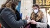 Люди в захисних масках дезинфікують руки на центральному залізничному вокзалі в Мілані, Італія