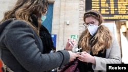 Люди в захисних масках дезинфікують руки на центральному залізничному вокзалі в Мілані, Італія