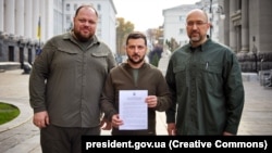 Parliament Speaker Ruslan Stefanchuk, Ukrainian President Volodymyr Zelenskiy, and Prime Minister Denys Shmyhal pose with a request for fast-track membership to the NATO military alliance in Kyiv on September 30, 2022.