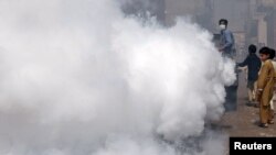 A man fumigates against mosquitoes in the streets of Lahore on September 9 as children look on.