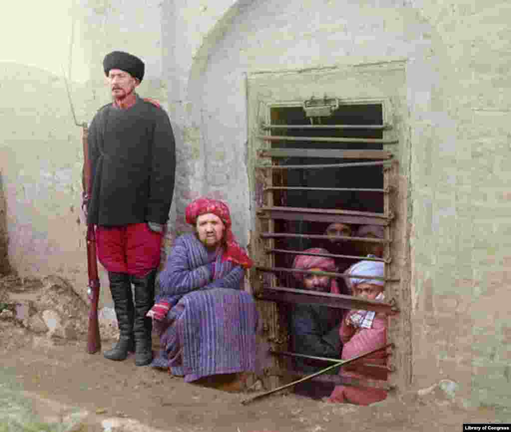 Inmates of a zindan -- a Central Asian prison -- are guarded by a man with a Russian-style uniform and boots.