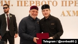 Адам Кадыров (слева), сын главы Чечни получает звание "почётного гражданина Курчалоевского района". Фотография из официального телеграм-канала Совета безопасности республики, опубликованная 14 августа 2026 г.